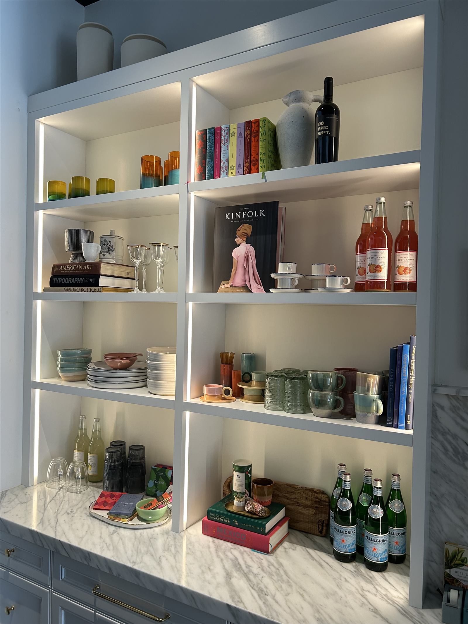 White built-in shelving styled with books, glassware, and bottles under integrated lighting