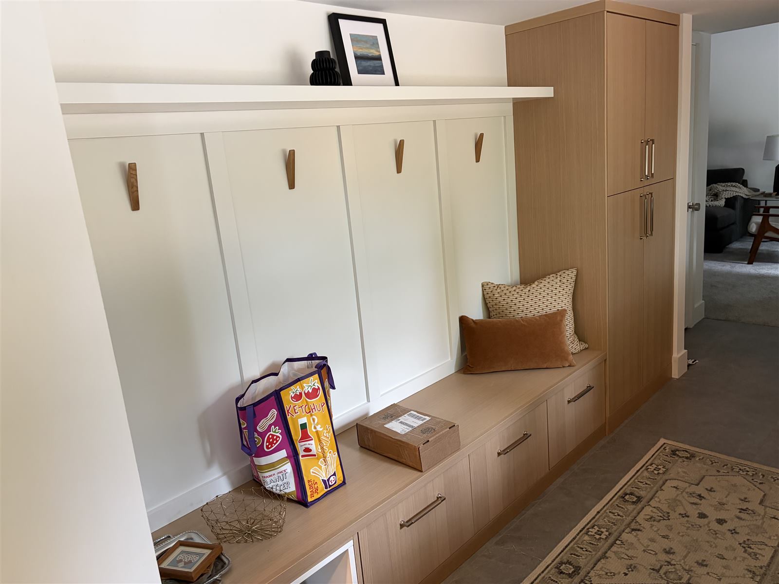 Built-in mudroom bench with wood coat hooks and a tall oak storage cabinet