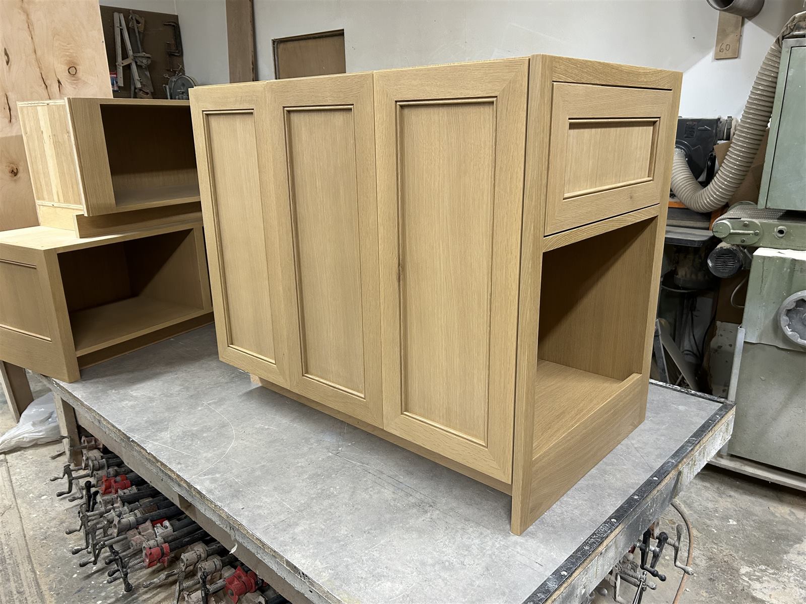 Unfinished oak cabinet on a workbench in the shop, surrounded by woodworking tools and clamps